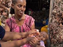 A mother smiles as her baby is vaccinated against polio in Ethiopia, showcasing local efforts to combat the disease.