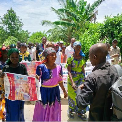 Women in a local community in DRC hold banners and posters during an awareness march against polio, raising attention for vaccination efforts.