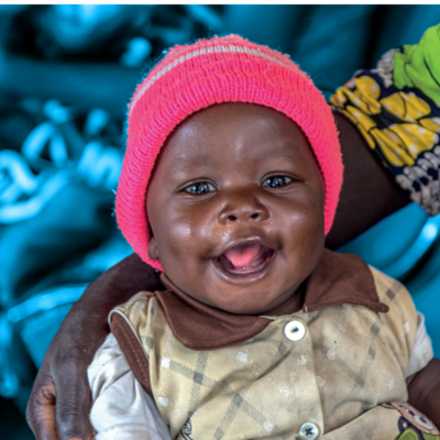 Smiling baby wearing a pink cap, held by a caregiver.