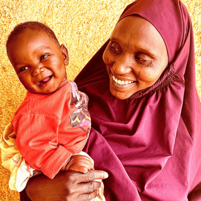 A smiling mother warmly holding her joyful baby, both radiating happiness against a vibrant yellow background.