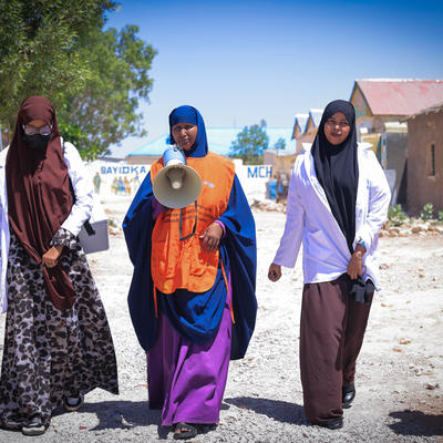 Three female UNICEF social mobilizers walk through a Somali community near a Maternal and Child Health (MCH) facility.
