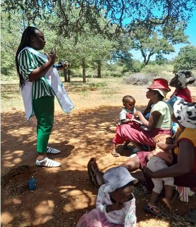 A health educator passionately discusses polio prevention with local families under the shade of trees in Beitbridge, Zimbabwe.
