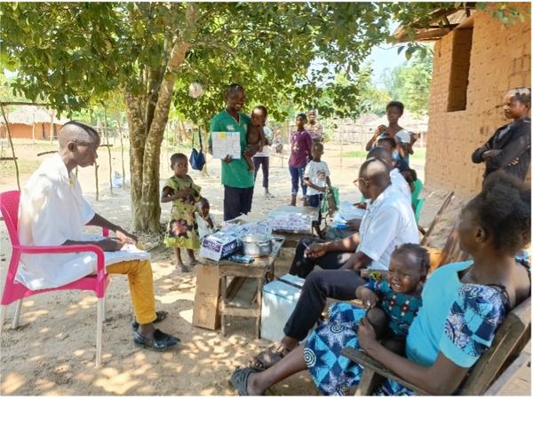 A community health worker explains polio vaccination efforts to local families under a tree, while others observe and listen attentively.