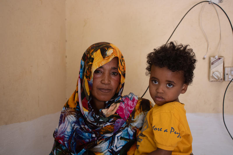A mother sits with her young child, awaiting a consultation or vaccination.