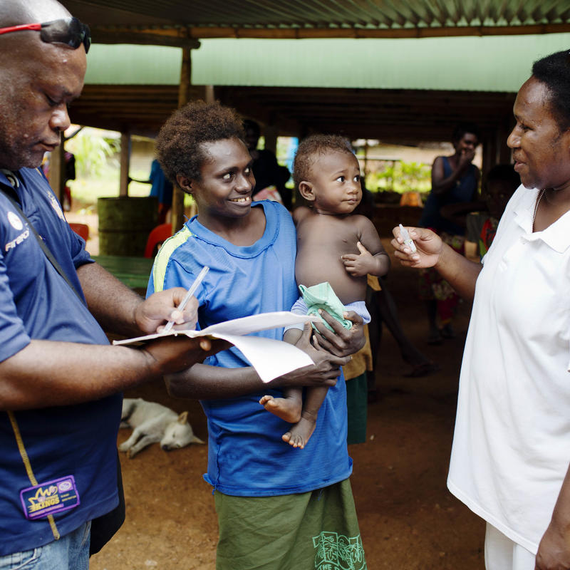 Woman holding her baby and talking to two Unicef representatives