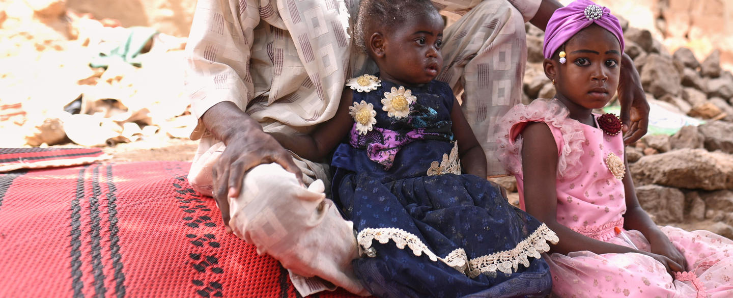 Two little girls sitting on the floor with their dad.