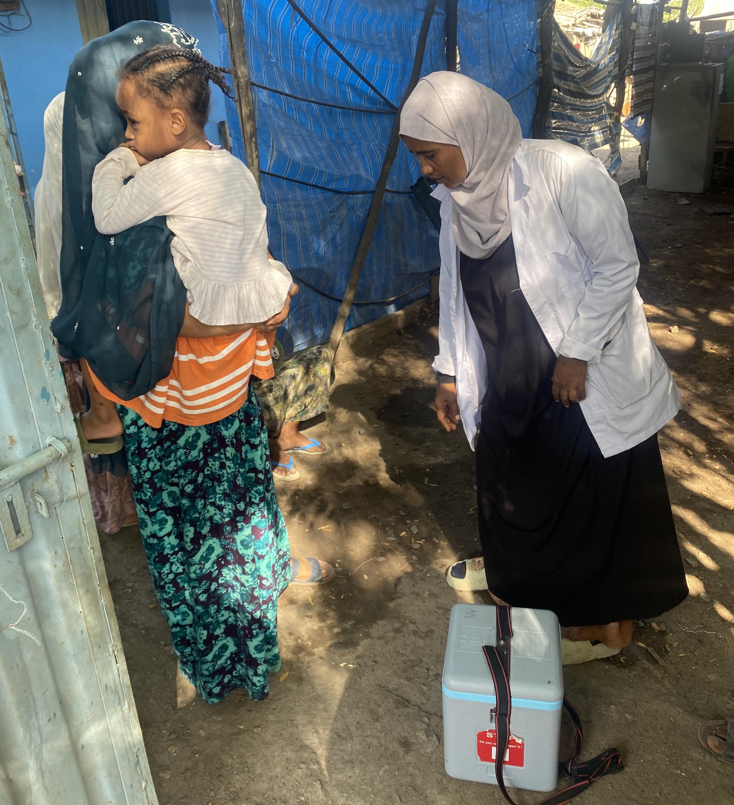 With a cold box of vaccines, Sister Mariyama Mohammed prepares to immunize a young child held by her mother. Her dedication ensures that Ethiopia’s health extension program reaches families directly, protecting children from preventable diseases.