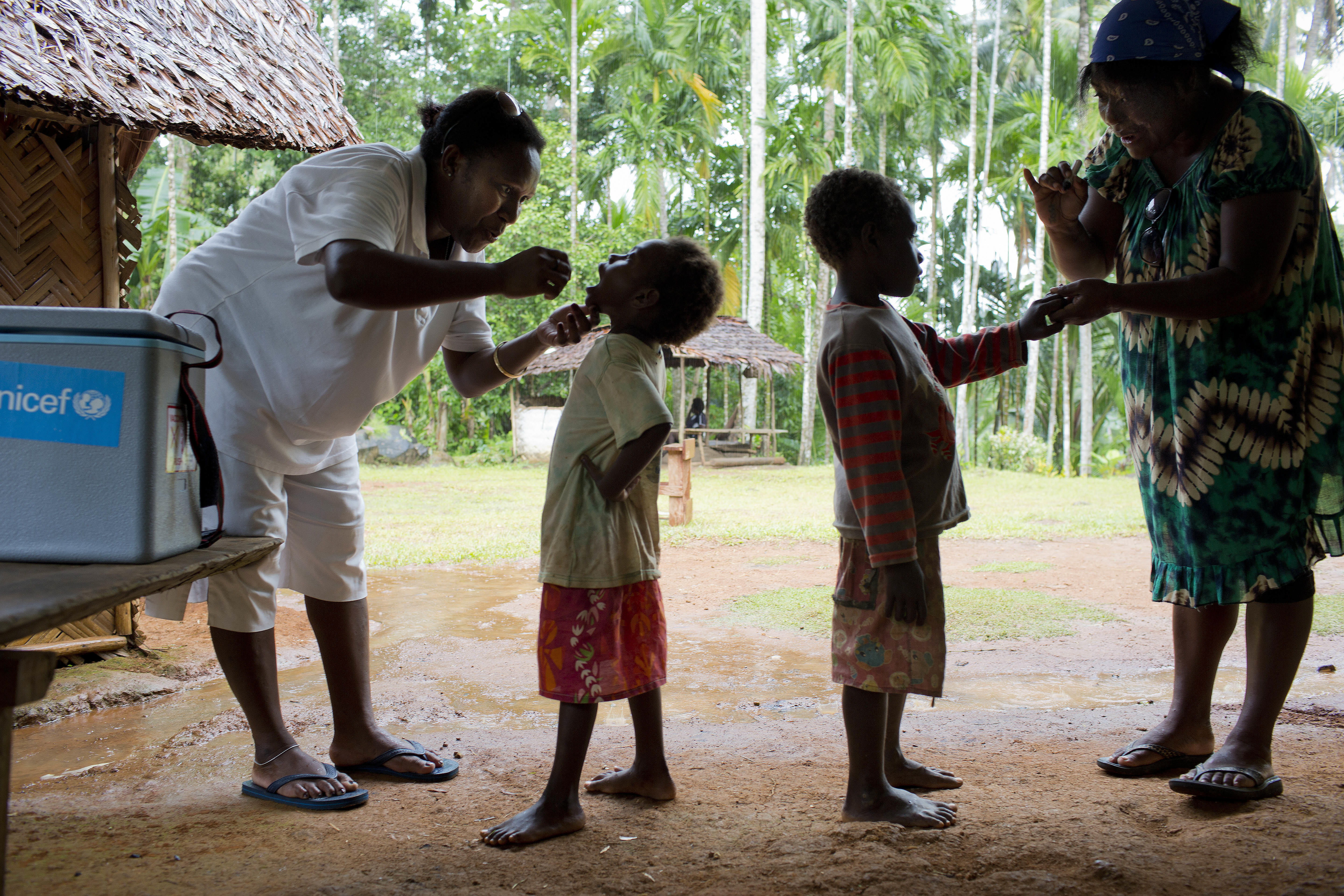 Two UNICEF representatives giving the polio vaccination to two kids.