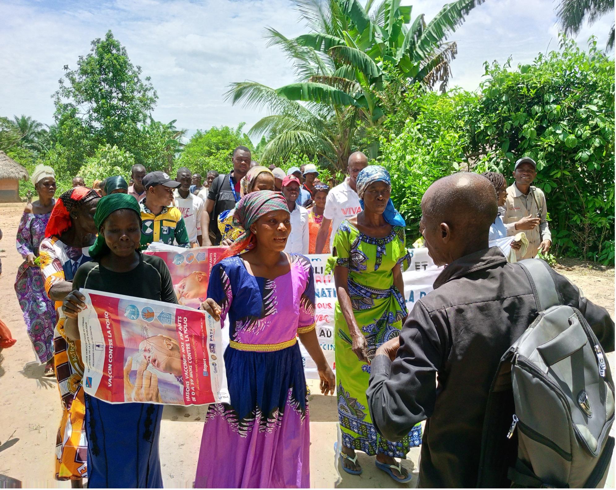Women in a local community in DRC hold banners and posters during an awareness march against polio, raising attention for vaccination efforts.